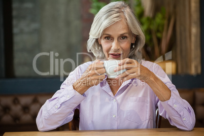 Portrait of senior female with coffee cup sitting at table