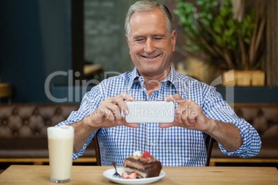 Smiling senior man photographing desert in plate at table