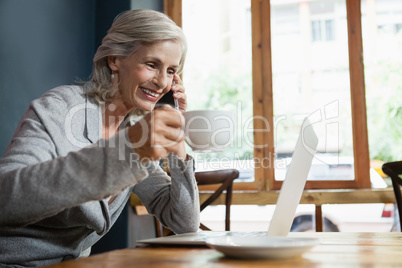 Smiling senior woman talking on mobile phone while drinking coffee