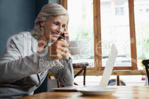 Smiling senior woman talking on mobile phone while drinking coffee