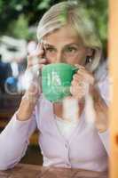 Senior woman drinking coffee while talking on mobile phone