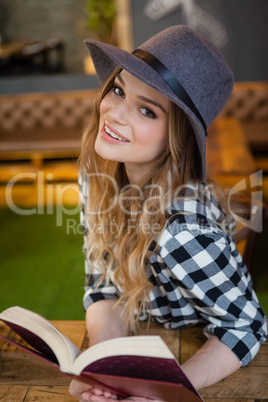 Woman wearing hat reading book while sitting in cafe shop