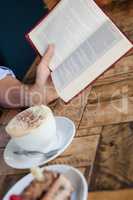 Cropped image of senior woman reading book while sitting by coffee cup