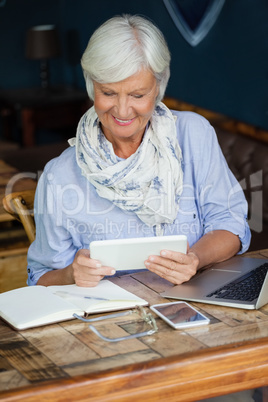 Smiling senior woman using digital tablet while sitting at table