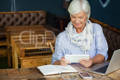 Woman using digital tablet while sitting at table in cafe