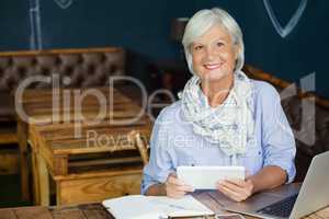 Portrait of smiling senior woman holding digital tablet while sitting at table