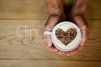 Person holding coffe cup with frothy art at wooden table