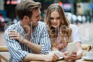 Couple using mobile phone while sitting at sidewalk cafe