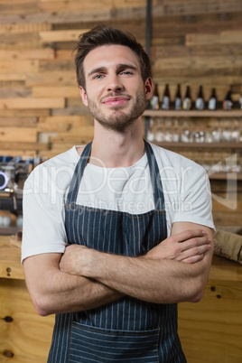 Portrait of smiling waiter standing with arms crossed