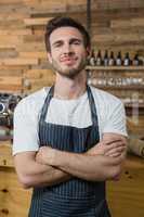 Portrait of smiling waiter standing with arms crossed