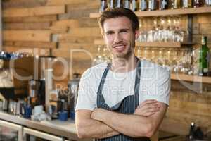 Portrait of smiling waiter standing with arms crossed at counter