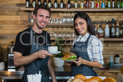 Portrait of waiter and waitresses holding cup of coffee and food at counter