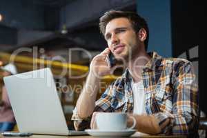 Young man talking on mobile phone while using laptop