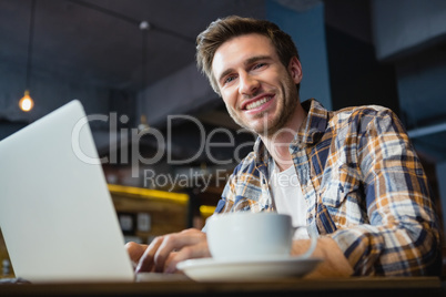 Portrait of happy young man using laptop while having coffee