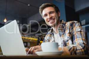 Portrait of happy young man using laptop while having coffee