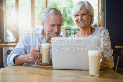 Senior couple using laptop while having coffee