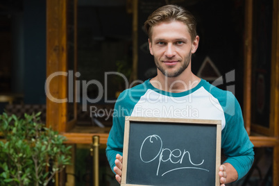 Portrait of smiling waiter holding chalkboard with open sign