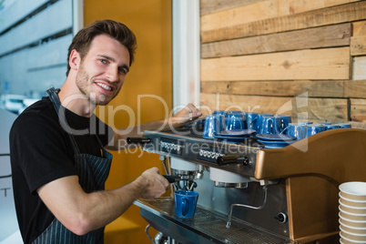 Portrait of smiling waiter making cup of coffee at counter