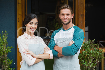 Portrait of smiling waiter and waitress standing with arms crossed