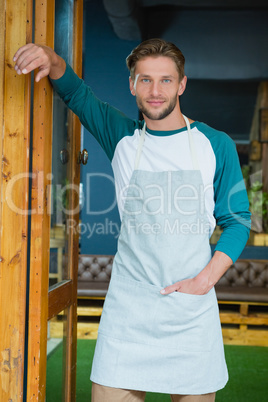 Portrait of smiling waiter standing with hand in pocket