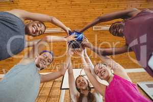 Smiling high school kids holding basketball together in the court