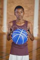 Confident high school boy holding basketball in the court