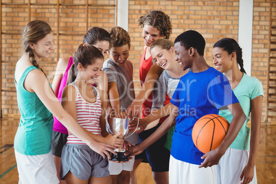 Excited high school kids holding trophy in basketball court