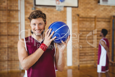 Smiling basketball player holding basketball in the court