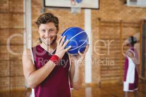 Smiling basketball player holding basketball in the court
