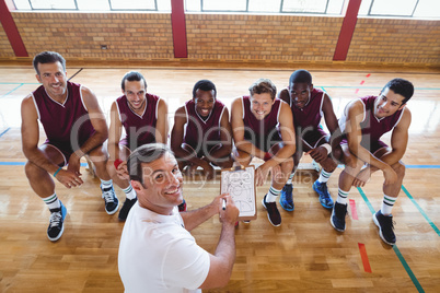 Smiling coach explaining game plan to basketball players