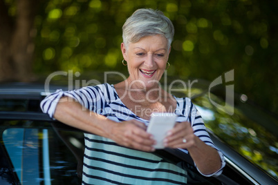 Senior woman using phone while leaning on car door
