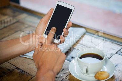 Woman holding mobile phone by coffee cup at table
