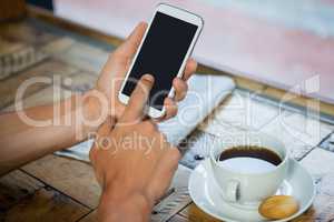 Woman holding mobile phone by coffee cup at table