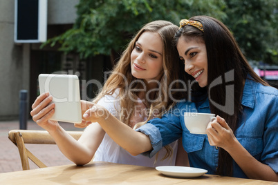 Smiling friends looking at tablet computer while sitting on chair