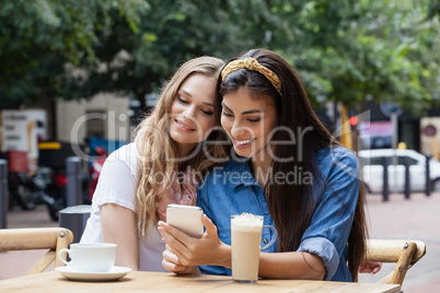Friends using mobile phone while sitting on chairs