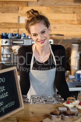 Portrait of cheerful owner standing by counter at cafe