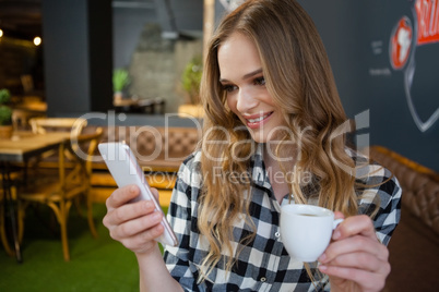 Smiling woman using mobile phone while holding coffee cup