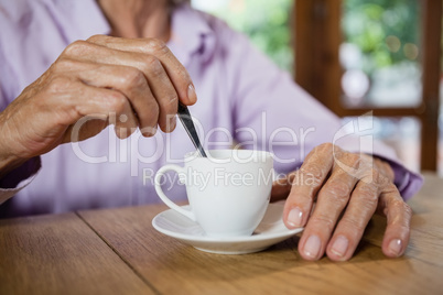 Midsection of senior woman stirring coffee