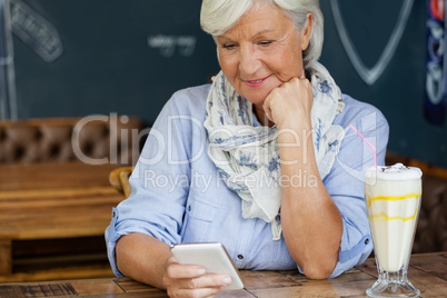 Senior woman using smart phone while sitting at table in cafe