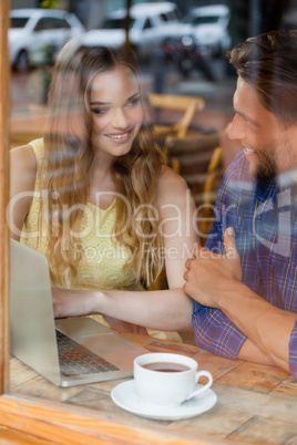 Smiling couple using digital laptop while sitting at cafe