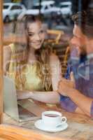 Smiling couple using digital laptop while sitting at cafe