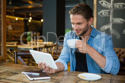 Smiling man using digital tablet while drinking coffee