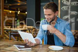Smiling man using digital tablet while drinking coffee