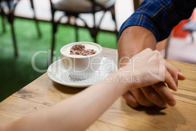 Couple holding hands by coffee cup on table