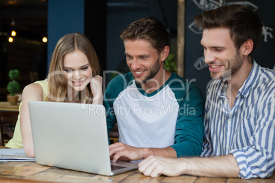 Happy friends looking at digital laptop while sitting on chair
