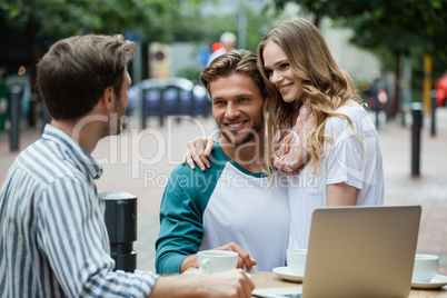 Couple looking at friend while sitting at sidewalk cafe