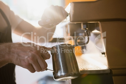 Mid section of waiter pouring milk in jug from coffee machine