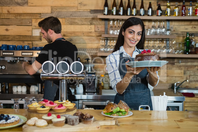 Portrait of smiling waitress holding a chocolate cake at counter