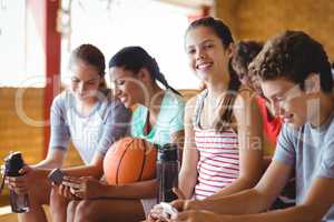 High school kids using mobile phone while relaxing in basketball court