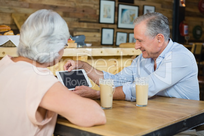 Senior couple using digital tablet while having coffee